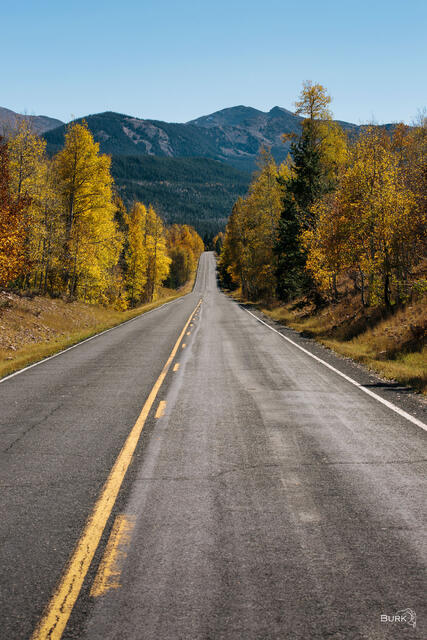 Autumn view of Mirror Lake Highway stretching through golden aspens toward the Uinta Mountains beneath a clear blue sky.
