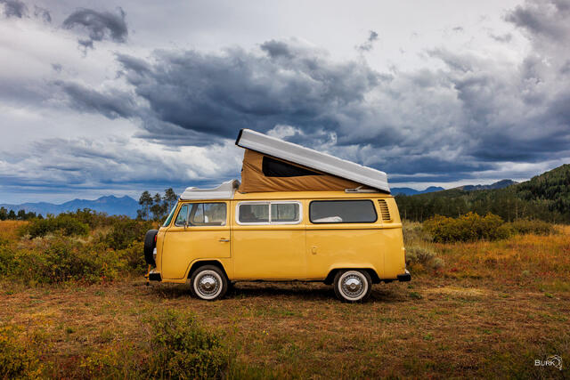 A yellow Volkswagen bus with a camper pop-up top, vintage.