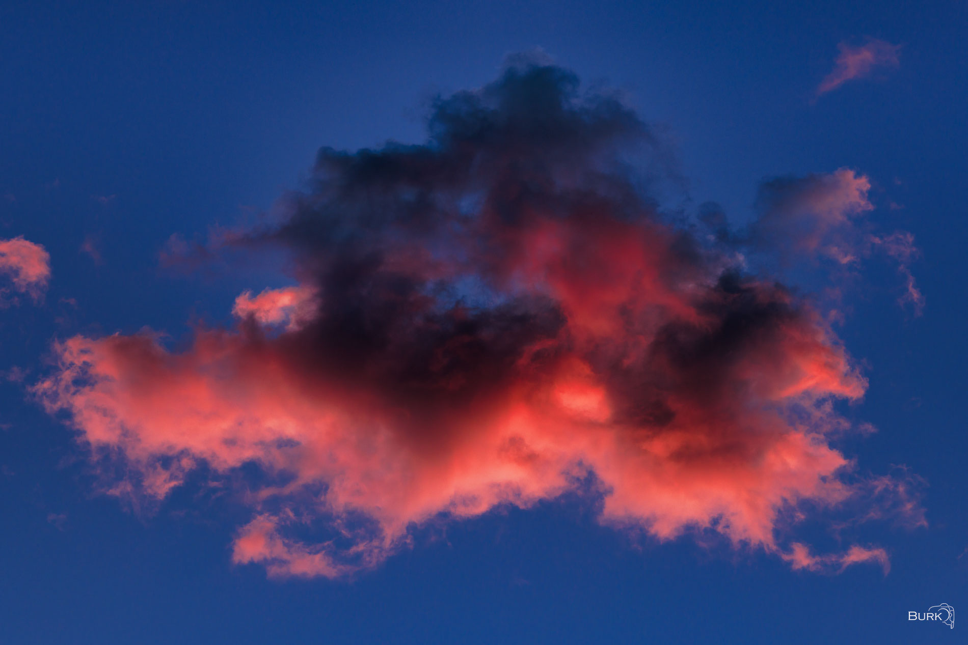 Illuminated Cloud Red-orange cloud illuminated by sunset light against a deep blue evening sky, with dark shadows adding dramatic contrast.